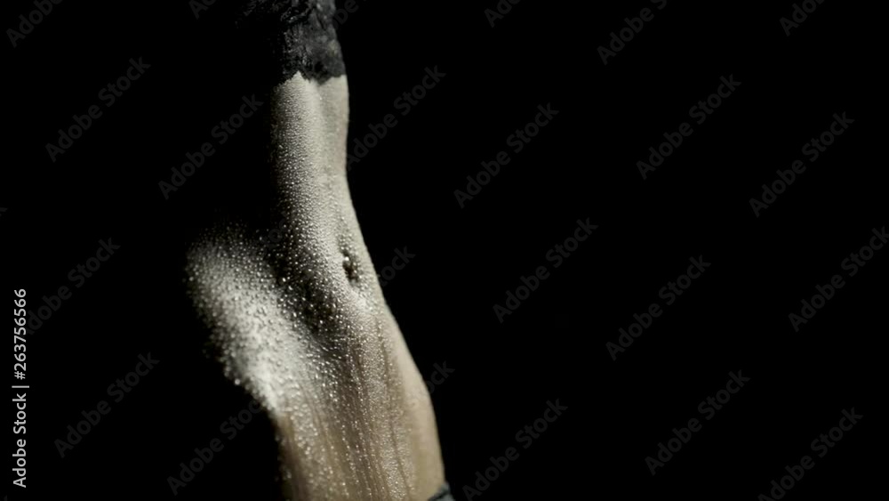 Close-up of a woman's toned abs as sweat drips down with dramatic lighting and black background