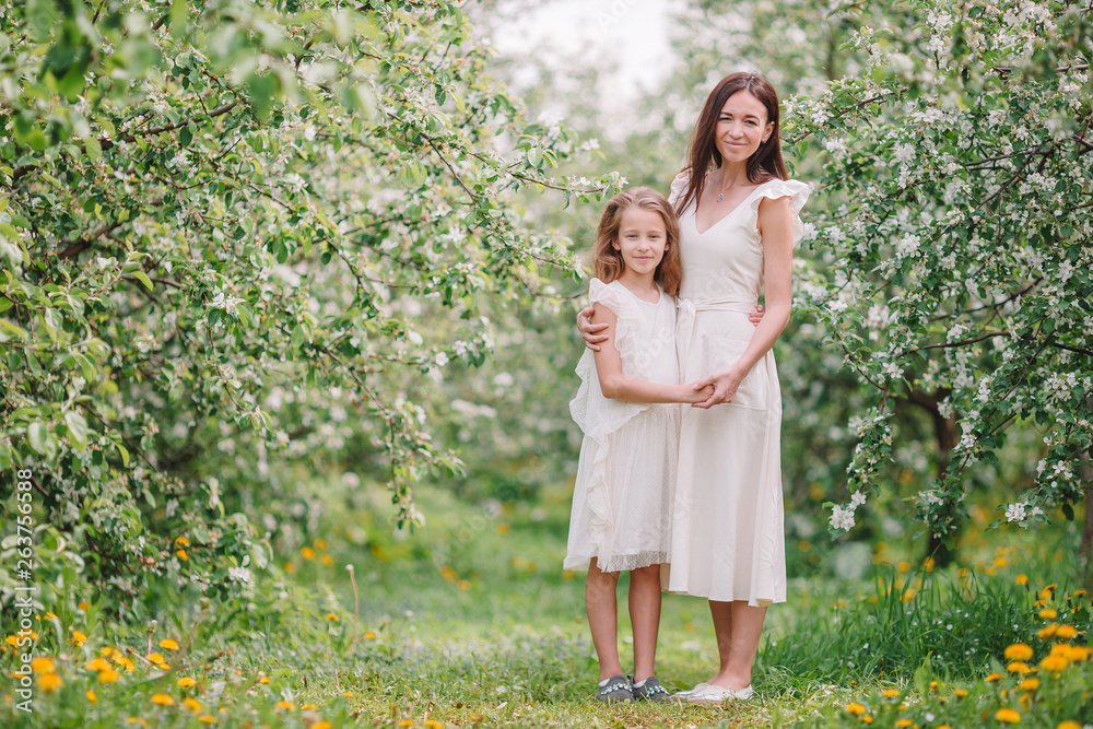 Fototapeta premium Adorable little girl with young mother in blooming cherry garden on beautiful spring day