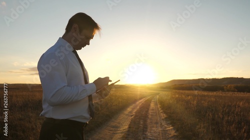 hands of man are driving their fingers over tablet. man checks email. Businessman working on tablet at sunset in park. agronomist works with the tablet in field. farmer on plantation with smartphone. © zoteva87