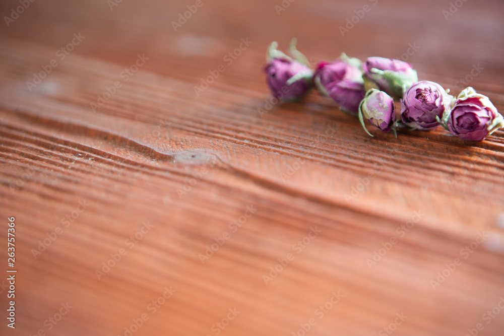 Small dry rosebuds lie on a background of aged wood of red-orange hue Small dry rosebuds lie on a background of aged wood of red-orange hue