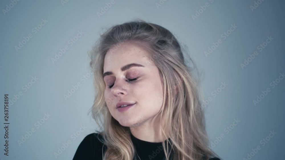 Gorgeous blond model girl is touching her hair and looking into camera flirting on a light blue background. Gorgeous blond model girl is touching her hair and looking into camera flirting on a light blue background.