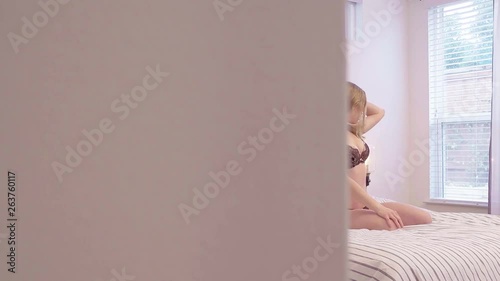 A sneaky view into a woman's bedroom as she strokes her hair suggestively on the bed 4K, 29.97 fps, slow motion.