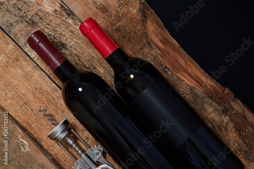 From above of arranged corkscrew and few bottle of red wine on wood above black background