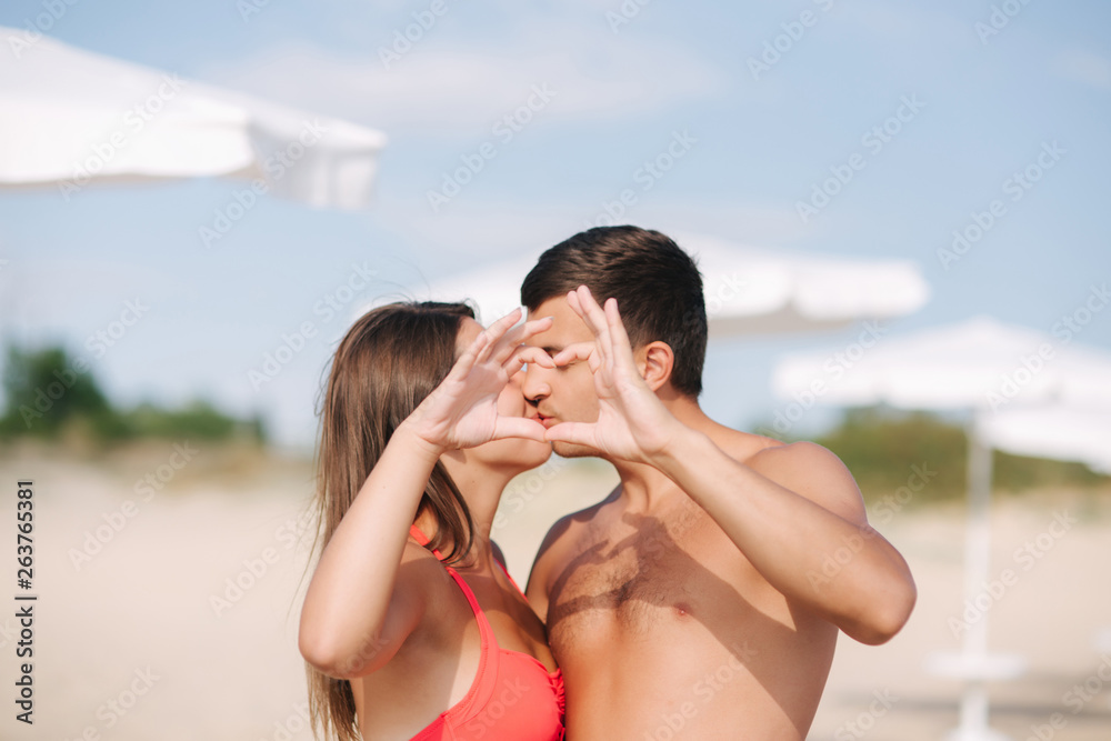 Happy couple make a heart. Woman and man on the beach. They kiss Happy couple make a heart. Woman and man on the beach. They kiss