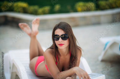 Beautiful lady in sunglasses lies on a sunbed in front of the pool © Aleksandr