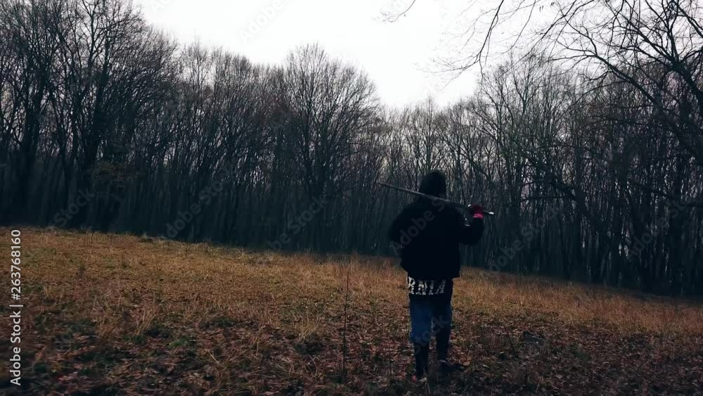 Man walks into a forest clearing with a long shiny sword over his shoulder. Guy swinging sword while walking alone through a wooded setting. Man walks into a forest clearing with a long shiny sword over his shoulder. Guy swinging sword while walking alone through a wooded setting.