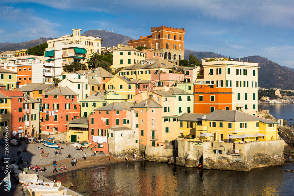 Multicolored amazing buildings with shutter windows in a small bay with boats, beach and sea food near the Mediterranean sea in Genoa Bocadasse marine, shore and mountains on the background.