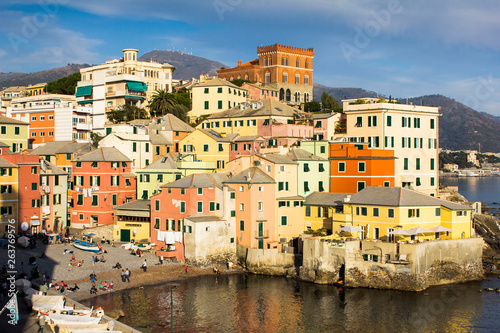 Multicolored amazing buildings with shutter windows in a small bay with boats, beach and sea food near the Mediterranean sea in Genoa Bocadasse marine, shore and mountains on the background.