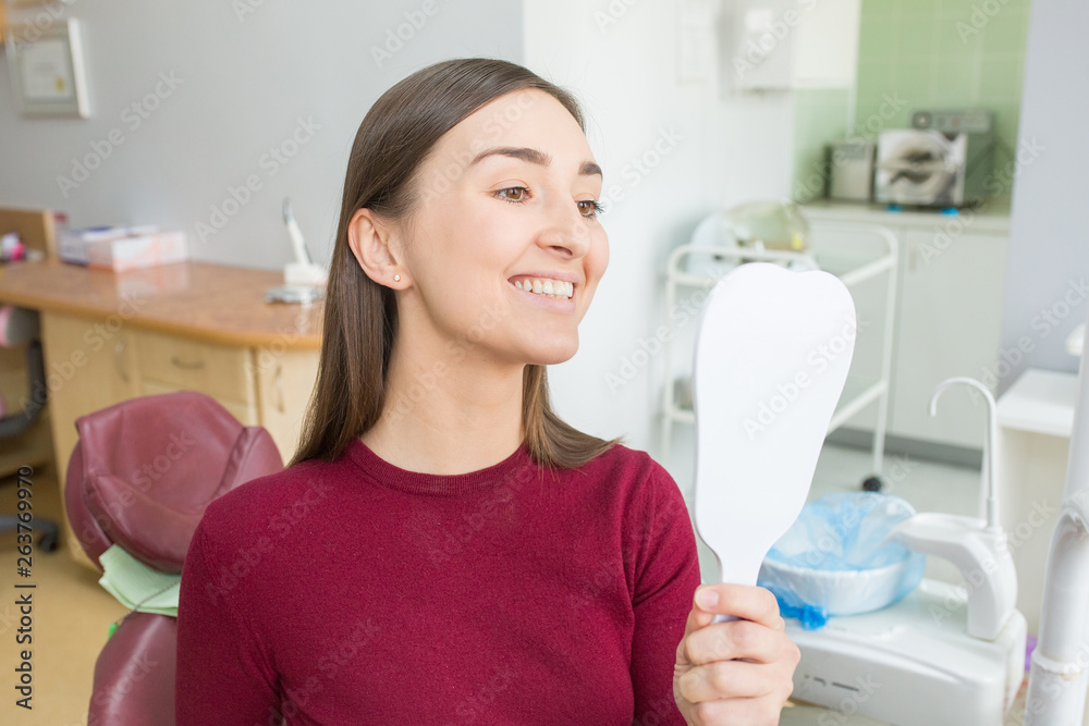 Young woman sits in a dental chair looking in mirror as a patient. People health care, dentistry, medicine concept. Doctor and patient. Teeth dentist with patient in hospital Young woman sits in a dental chair looking in mirror as a patient. People health care, dentistry, medicine concept. Doctor and patient. Teeth dentist with patient in hospital