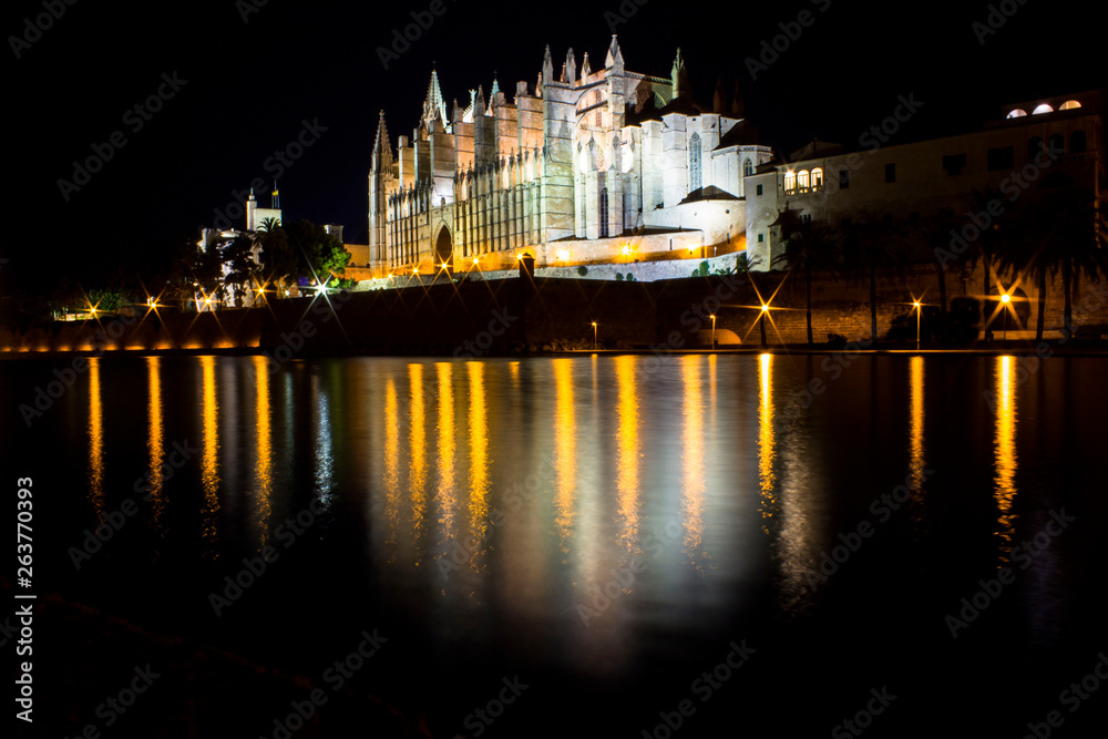 Illuminated spanish temple at night, white cathedral with beautiful reflection of it and lights illuminating main city cathedral. In Palma de Mallorca, Spain.