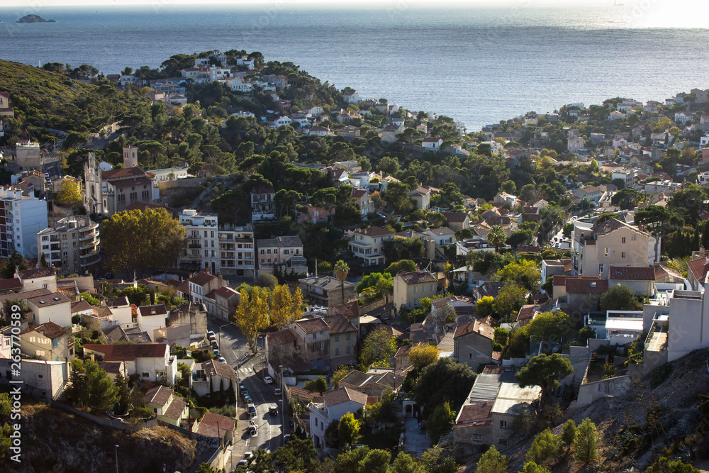 Obraz premium Cityscape and seascape of mediterranean sea from the top of the hill of Notre Dam de la Garde cathedral in Marseilles, Provence, France. Sunny port, harbour, brown tile roof tops.