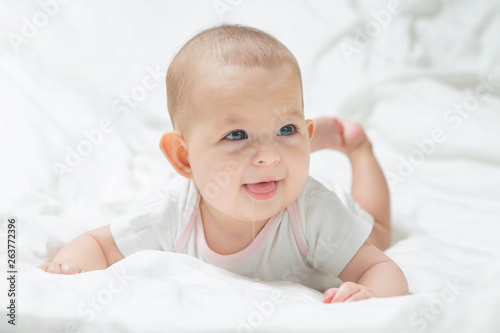 Increased salivation in the infant during teething. A baby girl in white clothes is lying on a white bed, smiling, drooling. Salivary glands activation