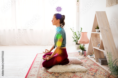 mindfulness, spirituality and healthy lifestyle concept - woman meditating in lotus pose at yoga studio with seven chakra symbols photo