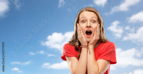 emotion, expression and people concept - shocked or scared teenage girl with open mouth in red t-shirt over blue sky and clouds background © Syda Productions