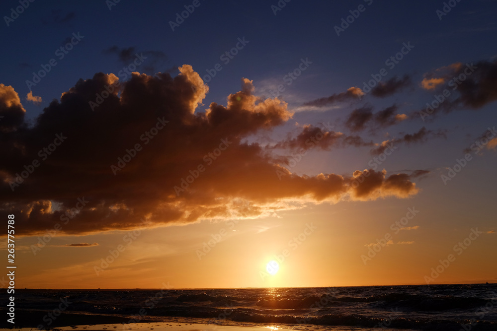 Dark sunset in with sun, sea, clouds and orange tones