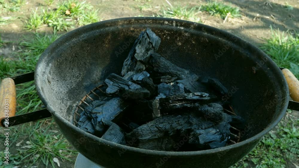 Human lights with match coal in metal grill or barbecue for burning outdoor on sunny summer day. Concept of outdoor recreation or a picnic on the weekend. Human lights with match coal in metal grill or barbecue for burning outdoor on sunny summer day. Concept of outdoor recreation or a picnic on the weekend.
