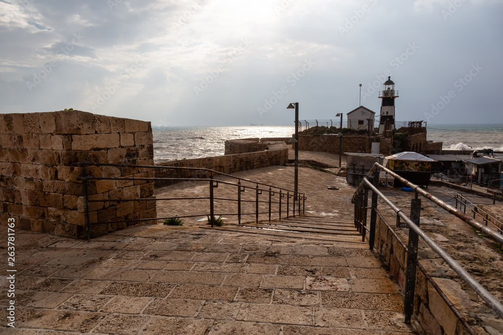 View of the Lighthouse on the Mediterranean Sea during a sunny and cloudy day. Taken at the Old City of Akko, Acre, Israel.