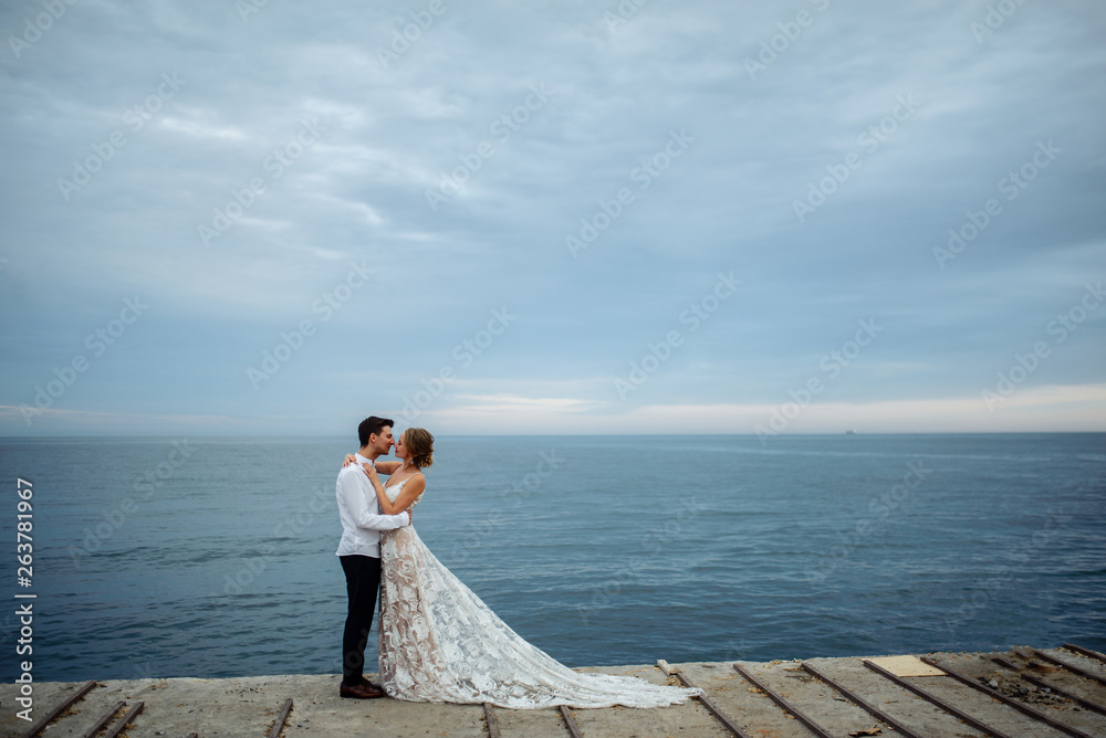 Happy young couple just married posing in classic luxury wedding clothes near the sea at sunset Happy young couple just married posing in classic luxury wedding clothes near the sea at sunset