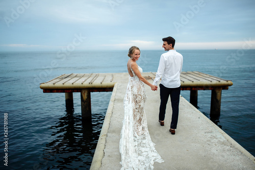 Happy young couple just married posing in classic luxury wedding clothes near the sea at sunset