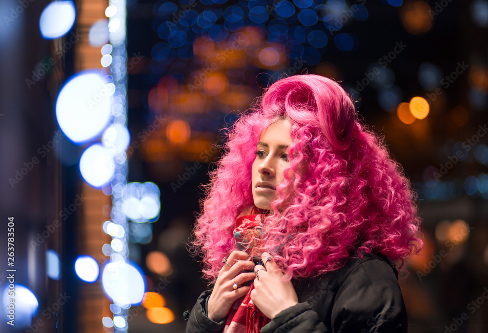 Portrait young attractive caucasian girl model with afro style curly bright pink hair, tattooed face. Evening downtown walking