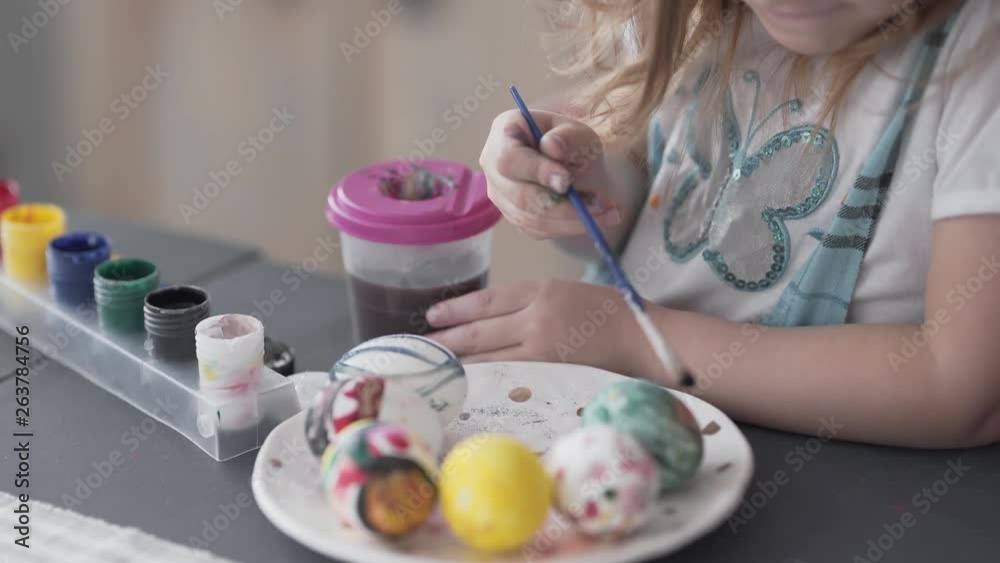 Close-up video of an adorable little girl who is sitting in a kitchen and painting an eggs on Easter. Girl is looking very concentrated on this process. Close-up video of an adorable little girl who is sitting in a kitchen and painting an eggs on Easter. Girl is looking very concentrated on this process.