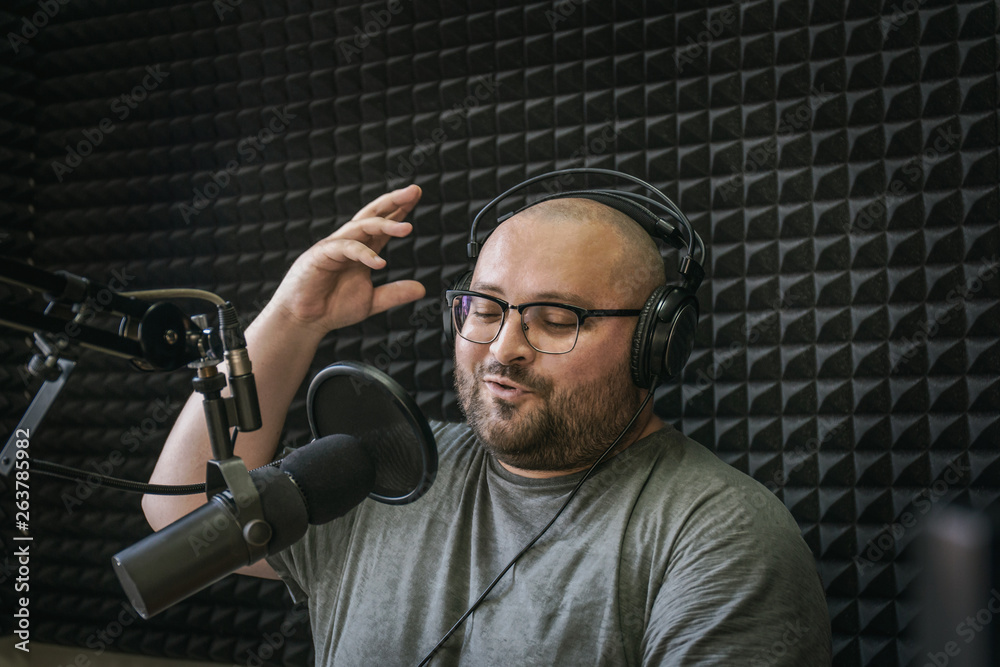 Smiling and gesturing radio host with headphones on his head reading news  from paper into studio microphone on radio station Stock Photo | Adobe Stock
