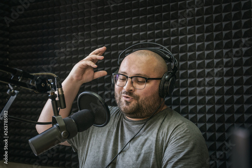 Obraz na plátně Smiling and gesturing radio host with headphones on his head reading news from p