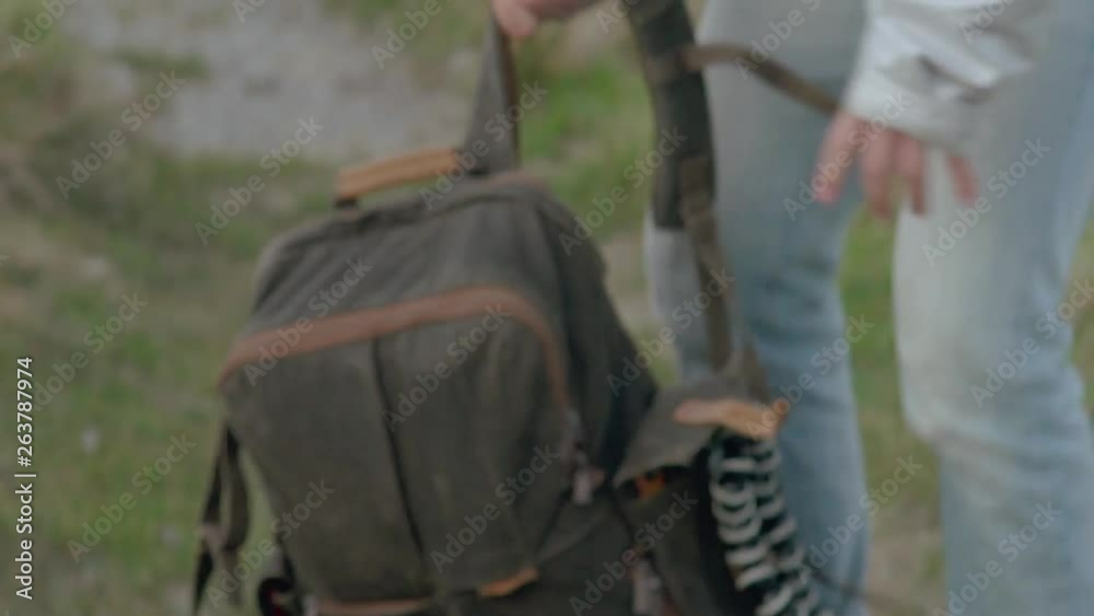 Young man packs up backpack with camera tripod and puts in on in daytime in slow motion
