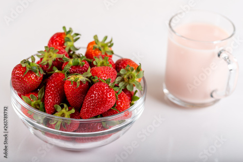 Fresh strawberry in a bowl and glass of milk on wooden background.