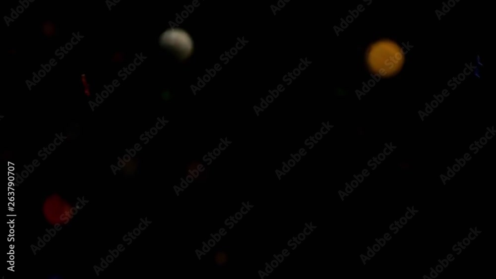 Multicolored confetti flying after being exploded, colorful rainbow stars and hearts particles bouncing against camera flying and falling down on black background. Top view close up macro slow motion