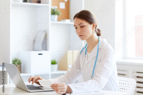 Portrait of young female doctor using laptop while working in office, copy space