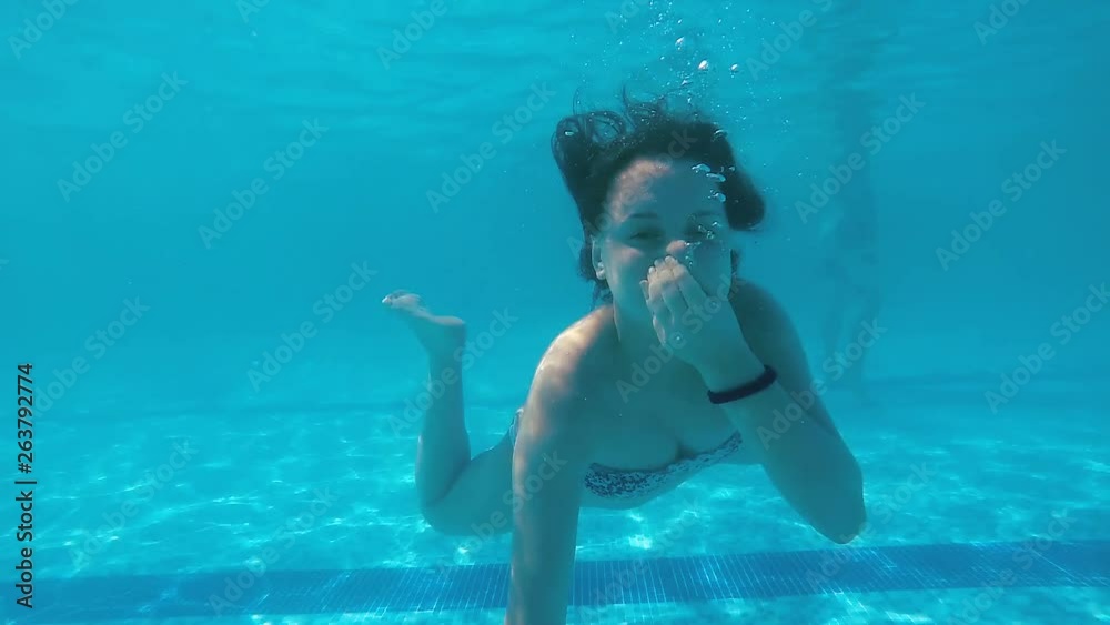 Attractive teen go swimming underwater in pool with clear water and posing to camera smiling and giving positive emotions, slow motion