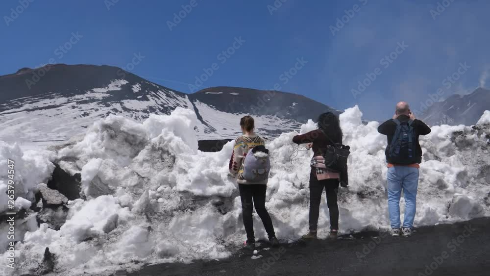 People standing by the snow on dirt road leading to main crater of Etna volcano in Sicily, Italy. On the right side seen top of the mount, cloud entering the scene