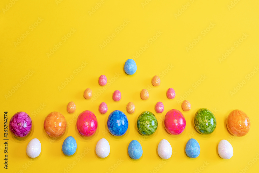 Obraz premium A lot of colorful Easter eggs on a yellow background. Top view, minimal Easter concept. Happy Easter card with free, empty space.