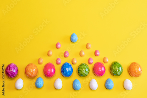 A lot of colorful Easter eggs on a yellow background. Top view, minimal Easter concept. Happy Easter card  with free, empty space. © Denys