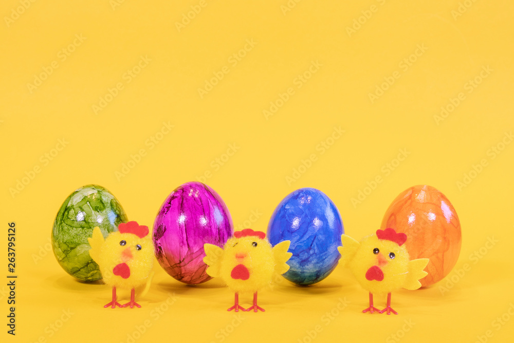 Four colored Easter eggs on a yellow background. Easter eggs stand in a row. In the foreground are yellow chicks. Happy Easter card  with free, empty space.