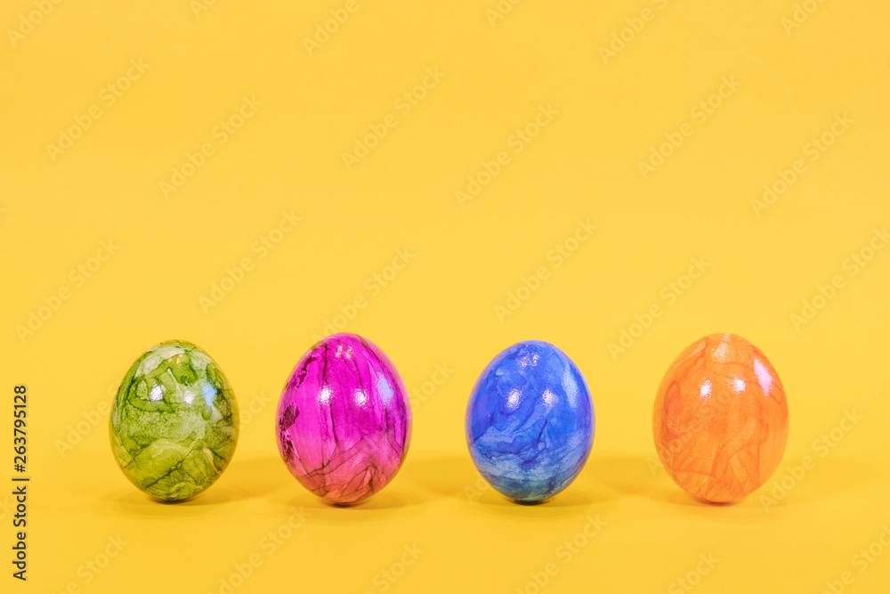 Four colored Easter eggs on a yellow background. Easter eggs stand in a row. Happy Easter card  with free, empty space.
