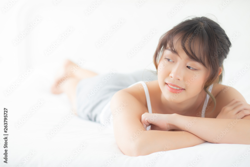 Beautiful portrait young asian woman lying and smile while wake up with sunrise at morning, beauty cute girl happy and cheerful resting on bed in the bedroom, lifestyle and relax concept.