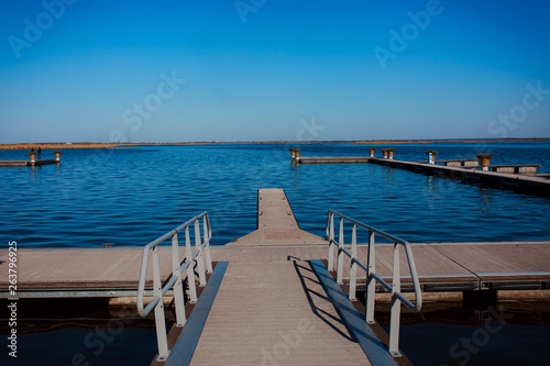 Coast pond. Water surface. Calm. Sunny weather. River bank. Pier. Recreation area. Decorative landscaping of the marina. © INTHEBLVCK