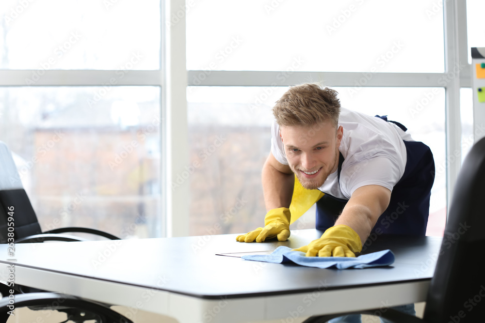 Male janitor cleaning table in office Male janitor cleaning table in office