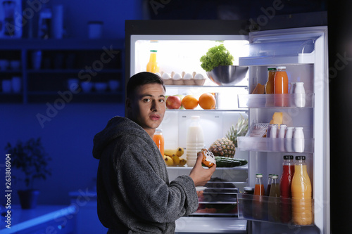 Φωτογραφία Afraid man caught in the act of eating unhealthy food near refrigerator at night
