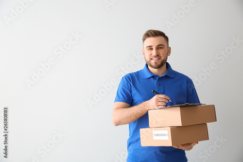 Handsome delivery man with boxes on light background