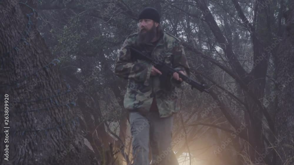 Tilt reveal from the ground showing a male hunter slowly walking in the woods with a weapon, 60 fps. Tilt reveal from the ground showing a male hunter slowly walking in the woods with a weapon, 60 fps.