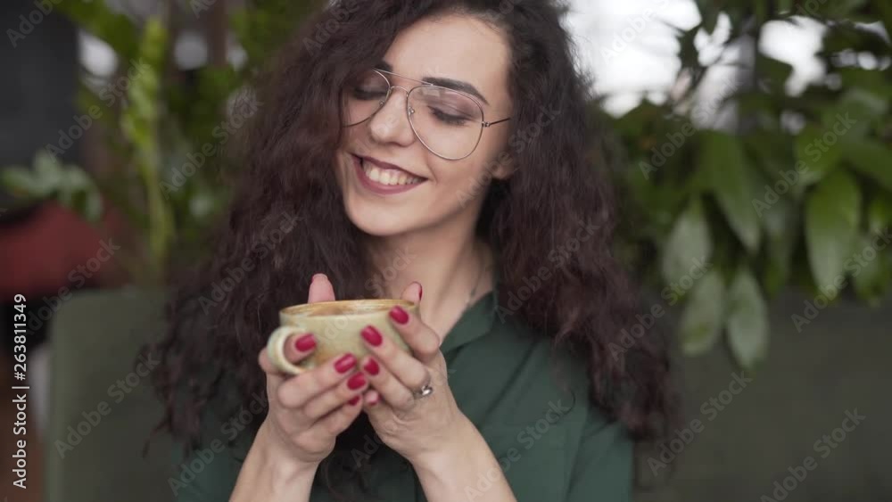 Young woman sipping on coffee and posing with a smile towards the camera, medium shot Young woman sipping on coffee and posing with a smile towards the camera, medium shot