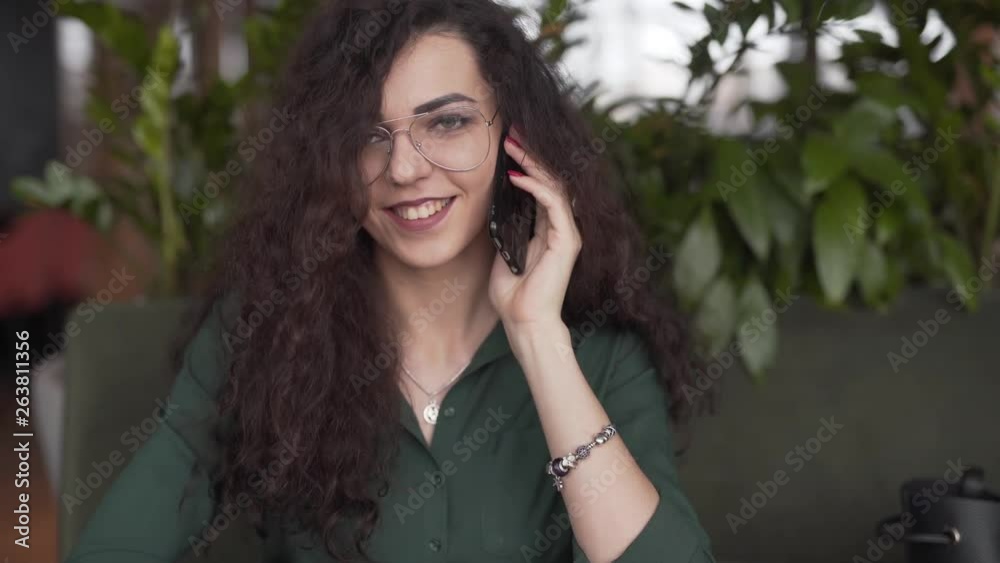 Shy young woman smiling and talking over the phone in a outdoor cafe, portrait shot