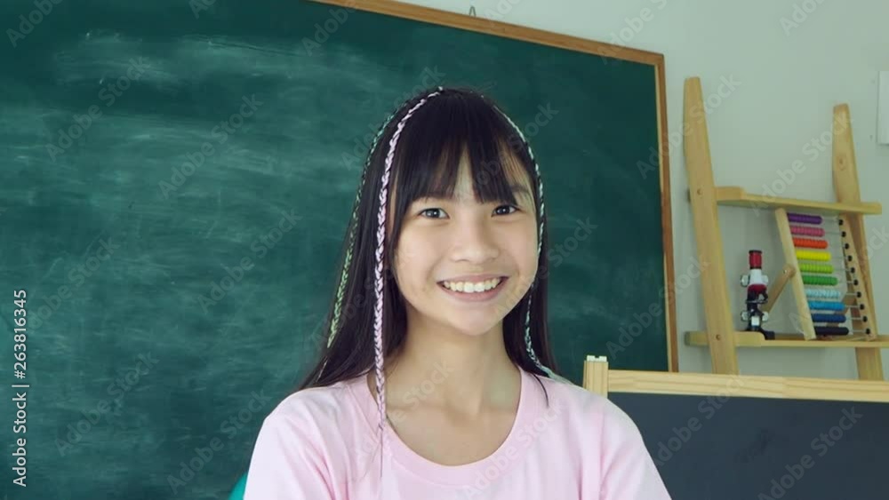Young asian schoolgirl standing and smiling in classroom