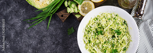 Healthy salad. Spring vegan salad with cabbage, cucumber, green onion and parsley on dark table. Banner. Top view