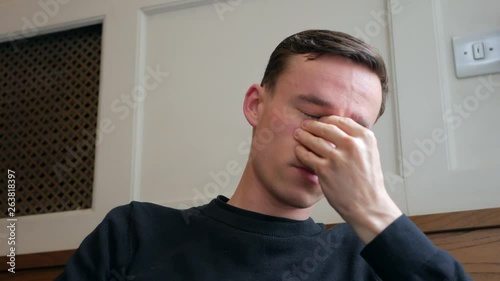 Tired young man rubbing his face and eyes with his hands