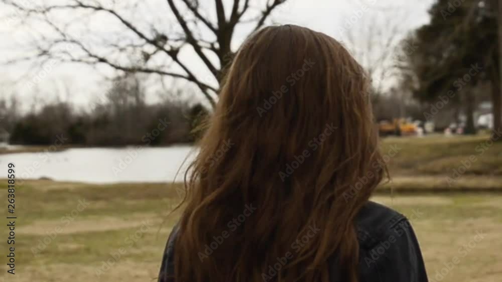 Steadicam shot of a beautiful,young, brunette college teenager walking on a trail in a city park wearing a white shirt with a black jacket. As she walks her hair is blowing in the wind. Steadicam shot of a beautiful,young, brunette college teenager walking on a trail in a city park wearing a white shirt with a black jacket. As she walks her hair is blowing in the wind.