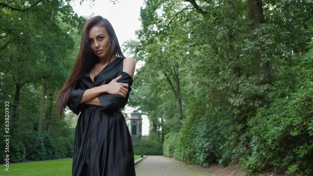 Brunette wearing a black dress and high heels walking in a national park in Belgium, surrounded by trees. Adjusting her hair while looking into the camera and to the side. Brunette wearing a black dress and high heels walking in a national park in Belgium, surrounded by trees. Adjusting her hair while looking into the camera and to the side.